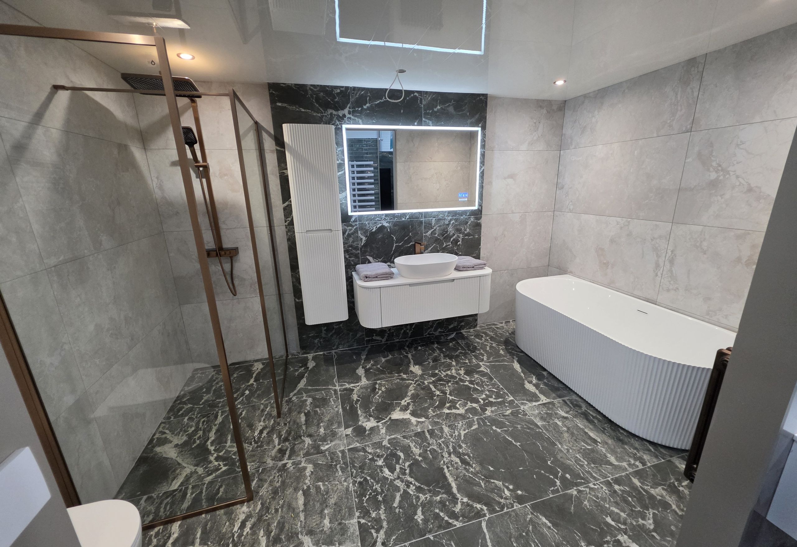 Bathroom display featuring black marble effect tiles, LED mirror and copper trim shower screen