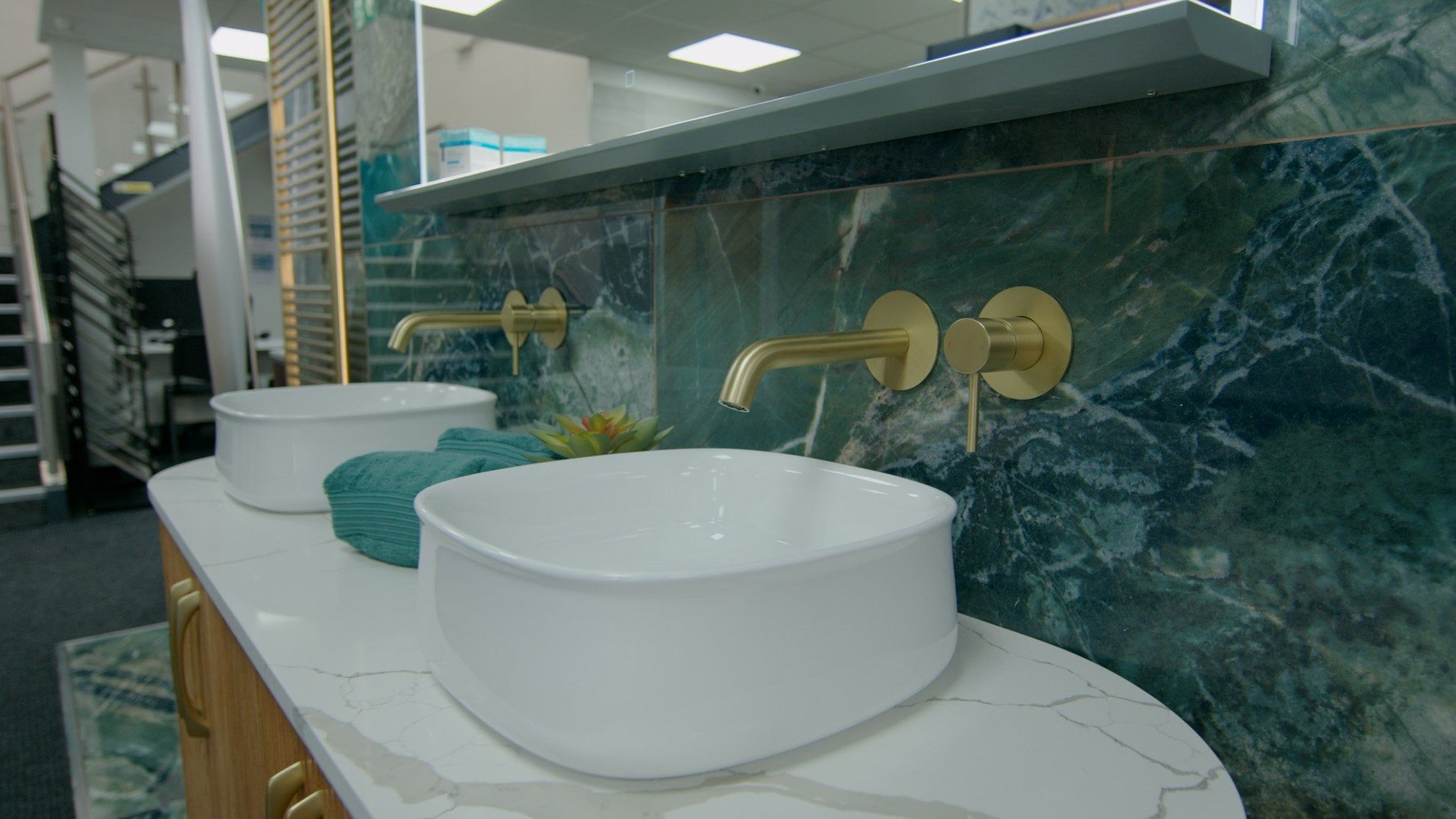 Showroom bathroom furniture display featuring modern counter top sinks, gold taps and emerald green marble tiles